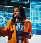 Public speaker doing presentation at tech forum event, explore ways emerging AI technologies can positively enhance companies workforce. Indian woman promoting artificial intelligence solutions