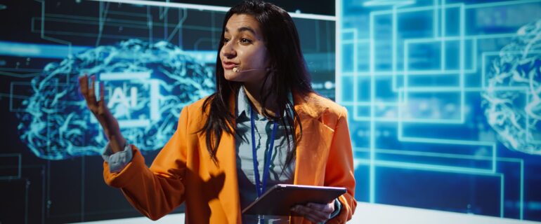 Public speaker doing presentation at tech forum event, explore ways emerging AI technologies can positively enhance companies workforce. Indian woman promoting artificial intelligence solutions